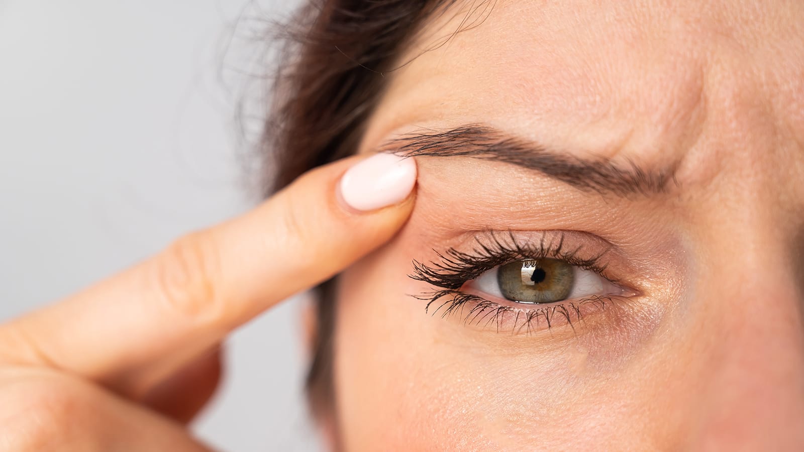 Close up portrait of Caucasian middle aged woman pointing to the wrinkles on the upper eyelid. Signs of aging on the face